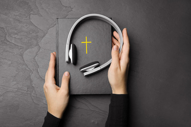 Photo of Woman with Bible and headphones at black table, top view. Religious audiobook