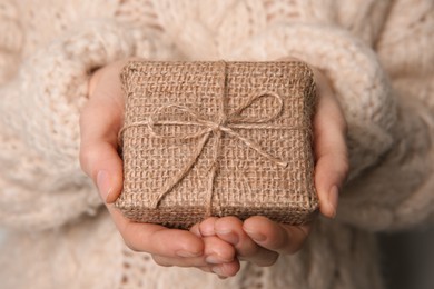 Photo of Woman in knitted sweater holding Christmas gift box, closeup