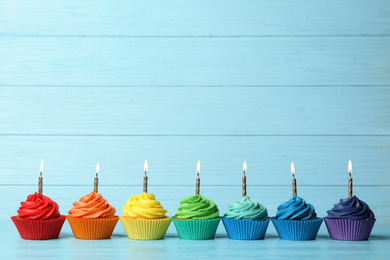 Delicious birthday cupcakes with burning candles on blue wooden table