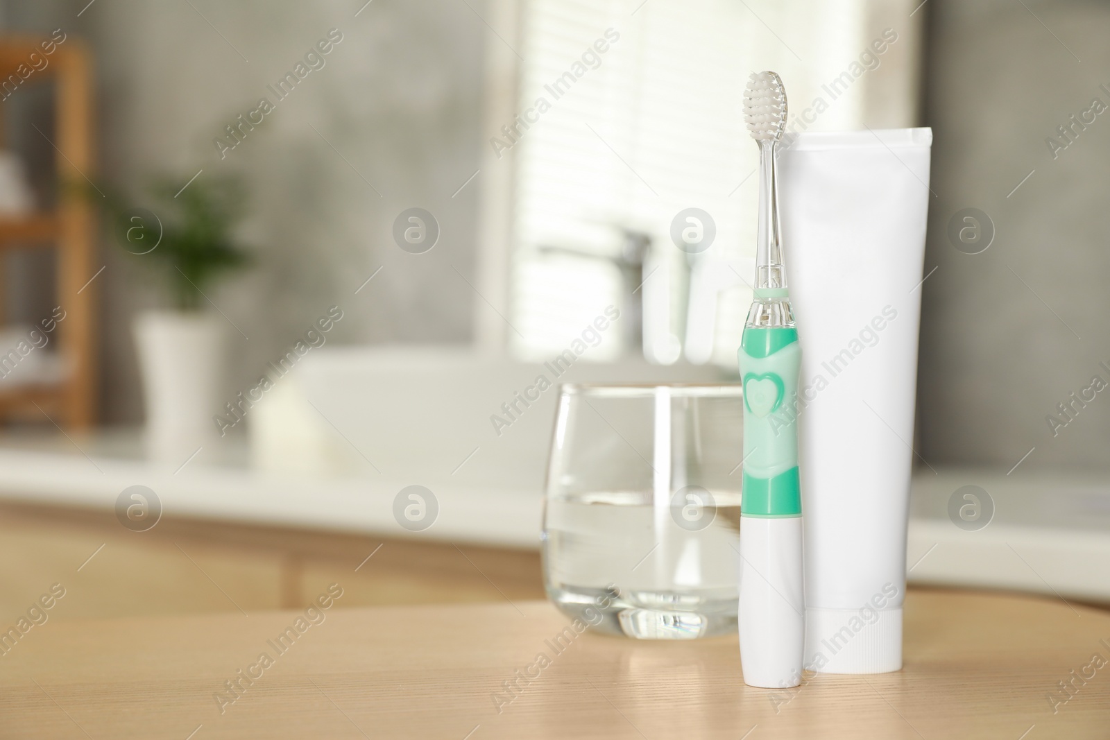 Photo of Electric toothbrush, tube with paste and glass of water on wooden table in bathroom. Space for text