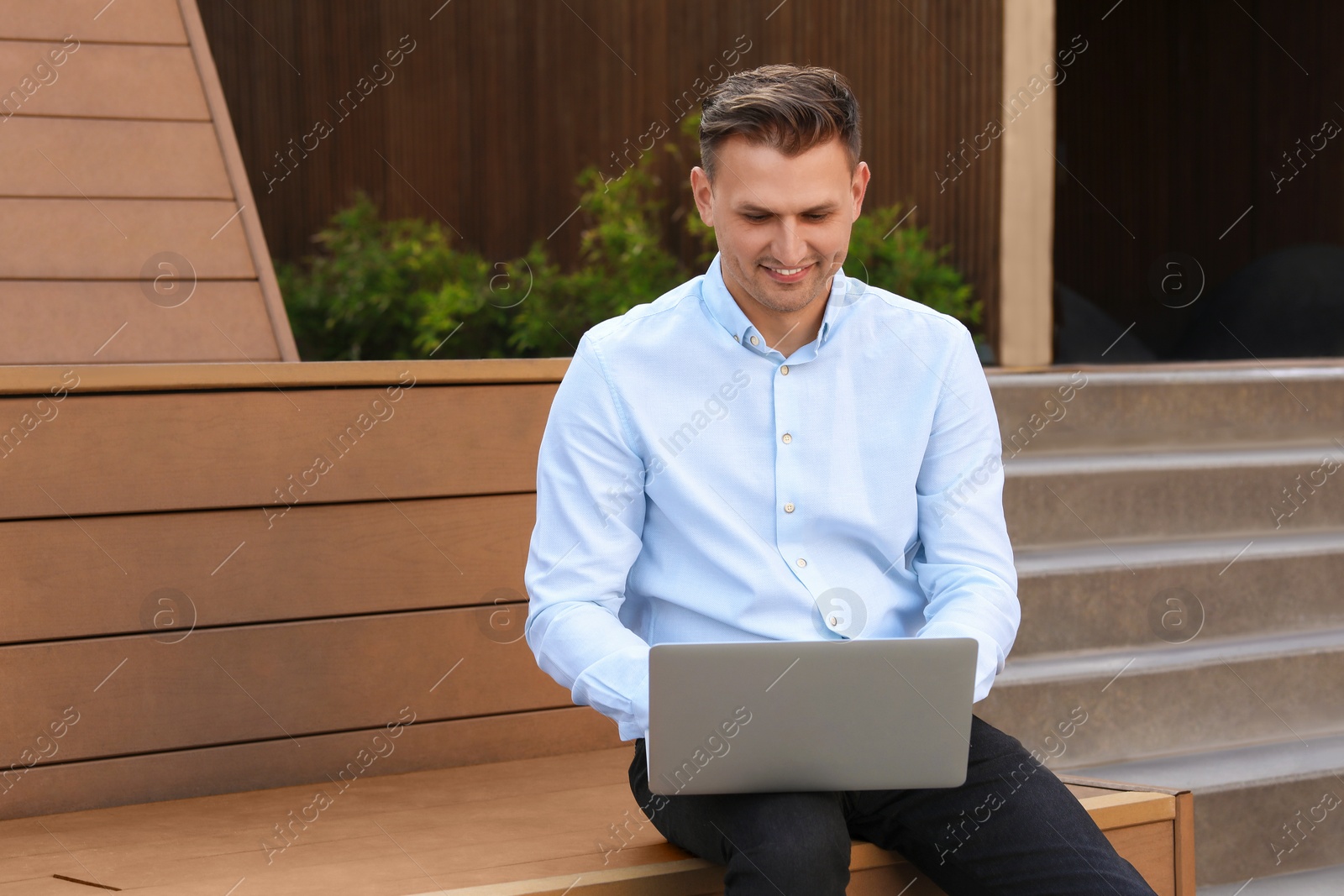 Photo of Handsome man using laptop on bench outdoors