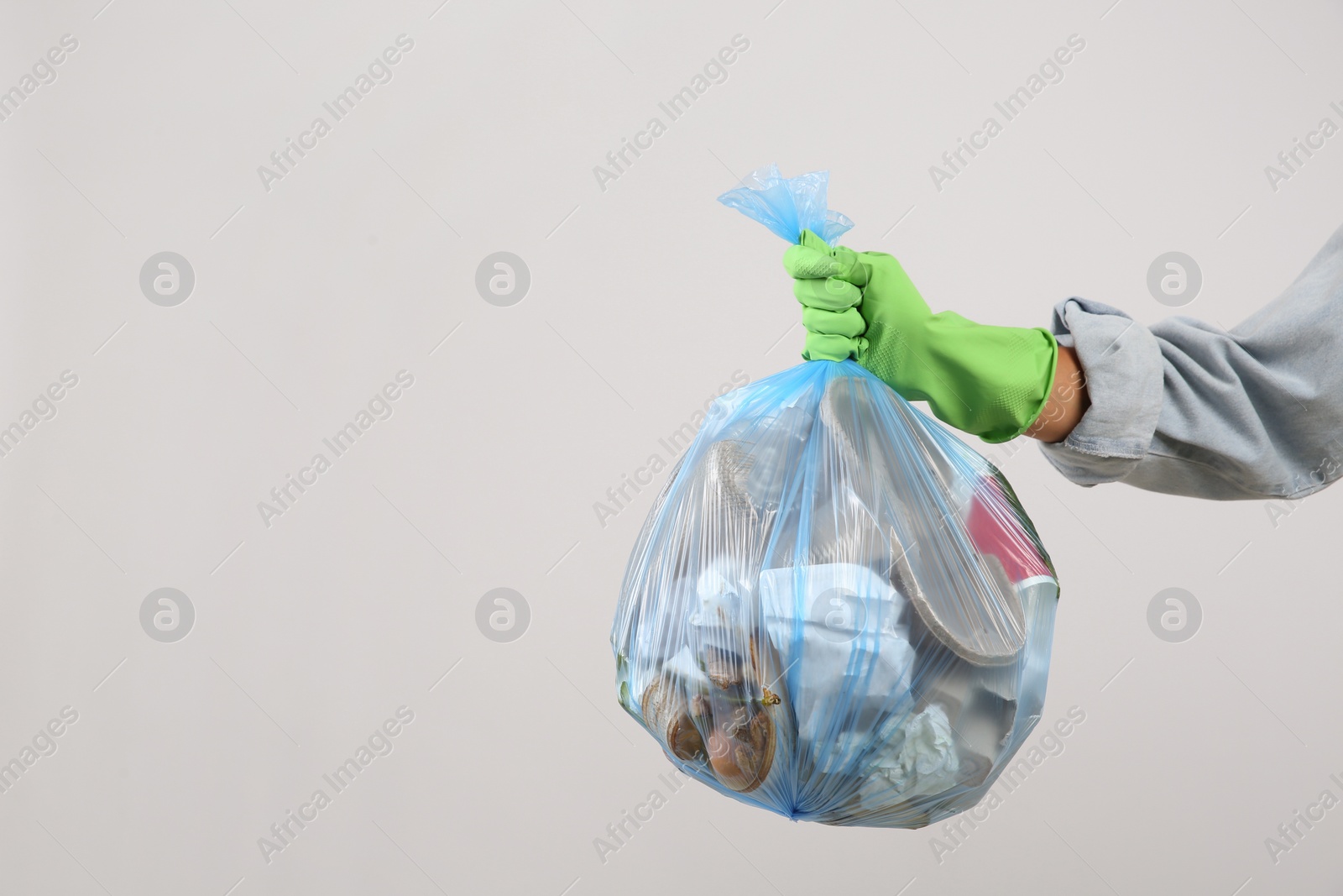 Photo of Woman holding full garbage bag on light background, closeup. Space for text