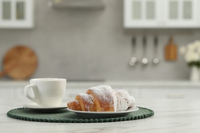 Croissant and cup of hot drink on white table in kitchen, space for text