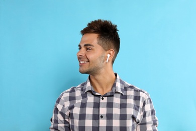 Photo of Happy young man listening to music through wireless earphones on light blue background