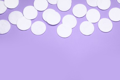 Many cotton pads on lilac background, flat lay. Space for text