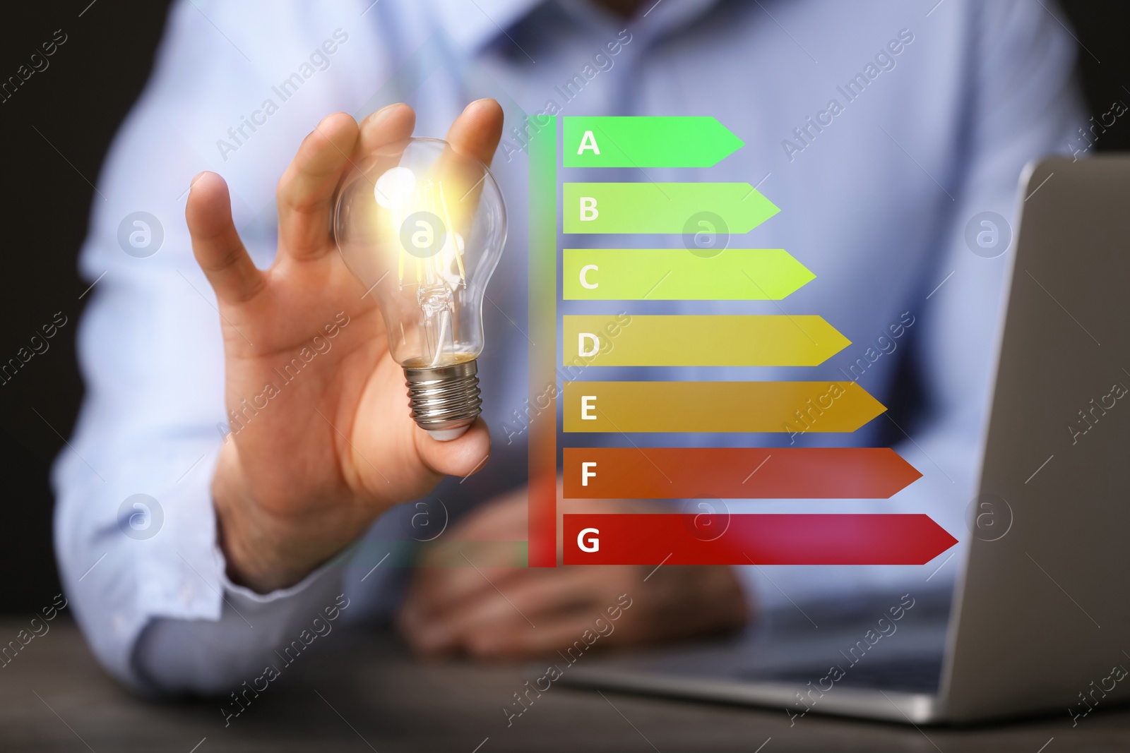 Image of Energy efficiency rating and man holding glowing light bulb at table, closeup