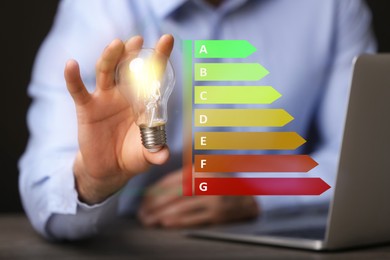 Image of Energy efficiency rating and man holding glowing light bulb at table, closeup