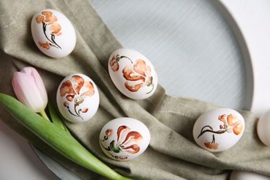 Photo of Beautifully painted Easter eggs and tulip on white table, top view