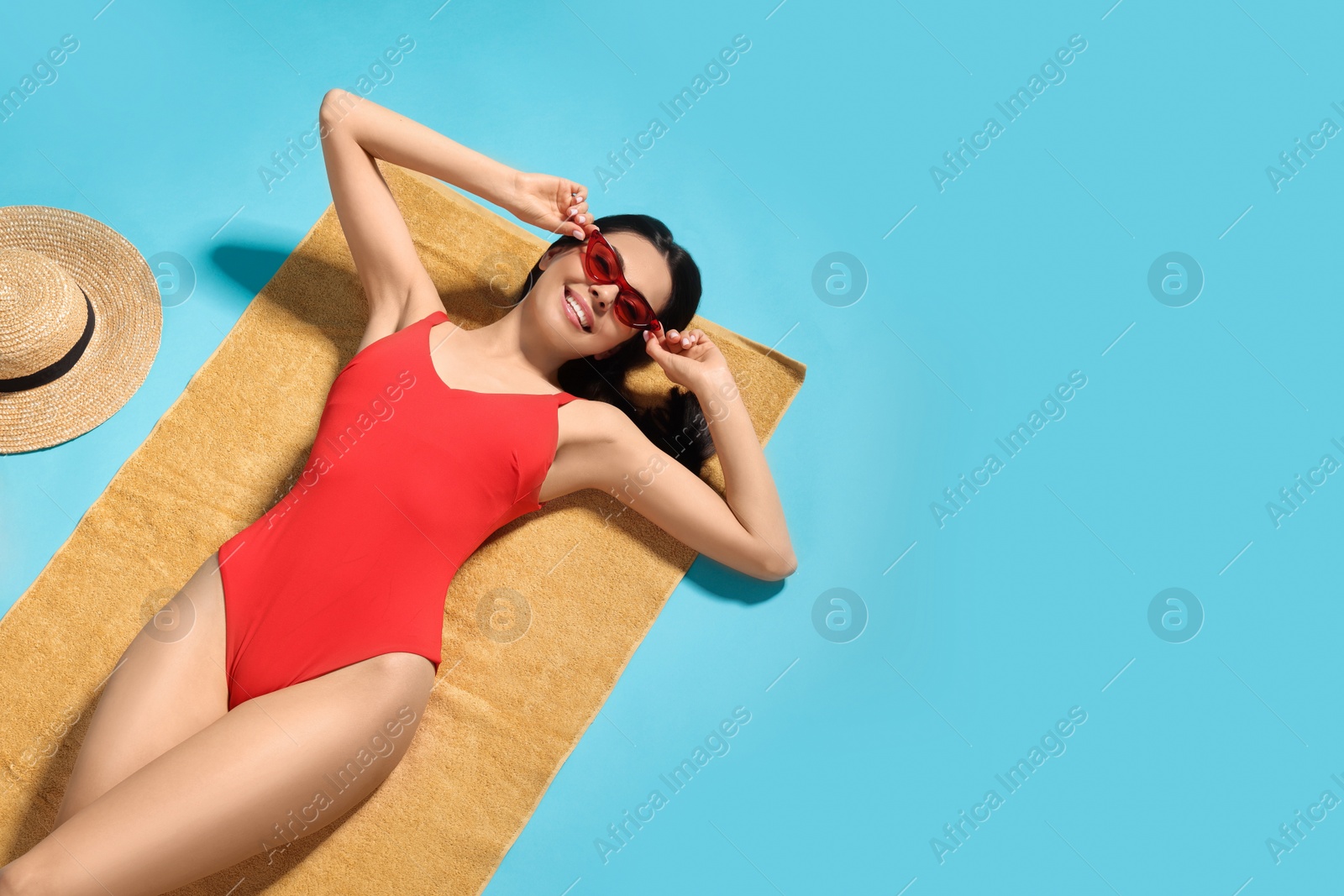 Photo of Young woman in stylish swimsuit on beach towel against light blue background. Space for text