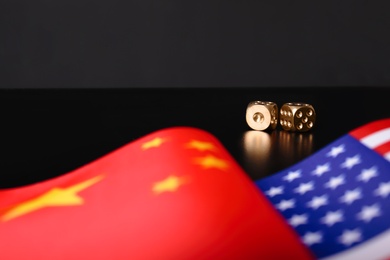 USA and China flags with dices on black table. International relations