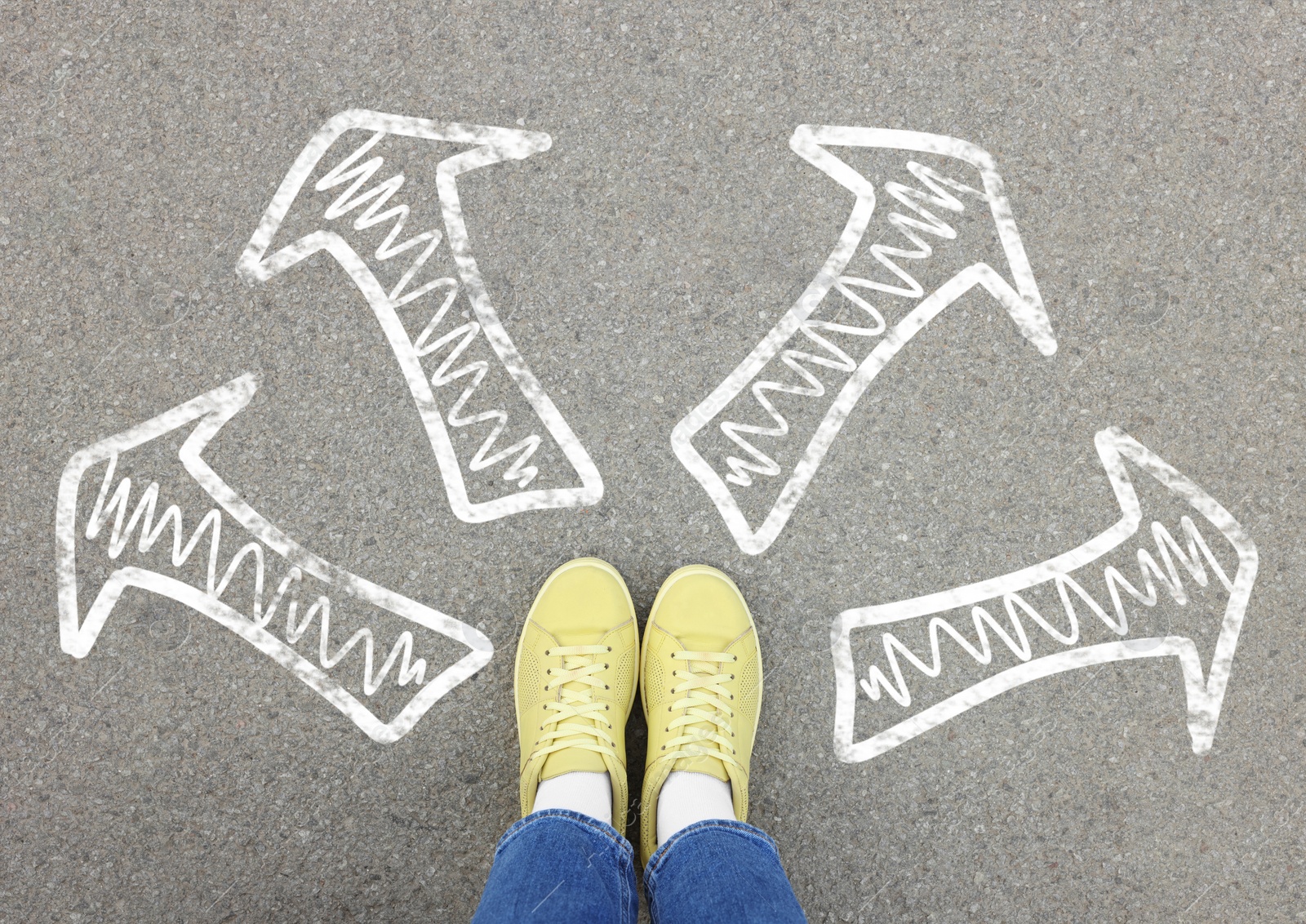 Image of Choosing future profession. Girl standing in front of drawn signs on asphalt, top view. Arrows pointing in different directions symbolizing diversity of opportunities