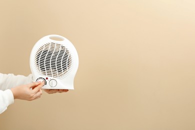 Photo of Young woman holding electric fan heater on beige background, closeup. Space for text