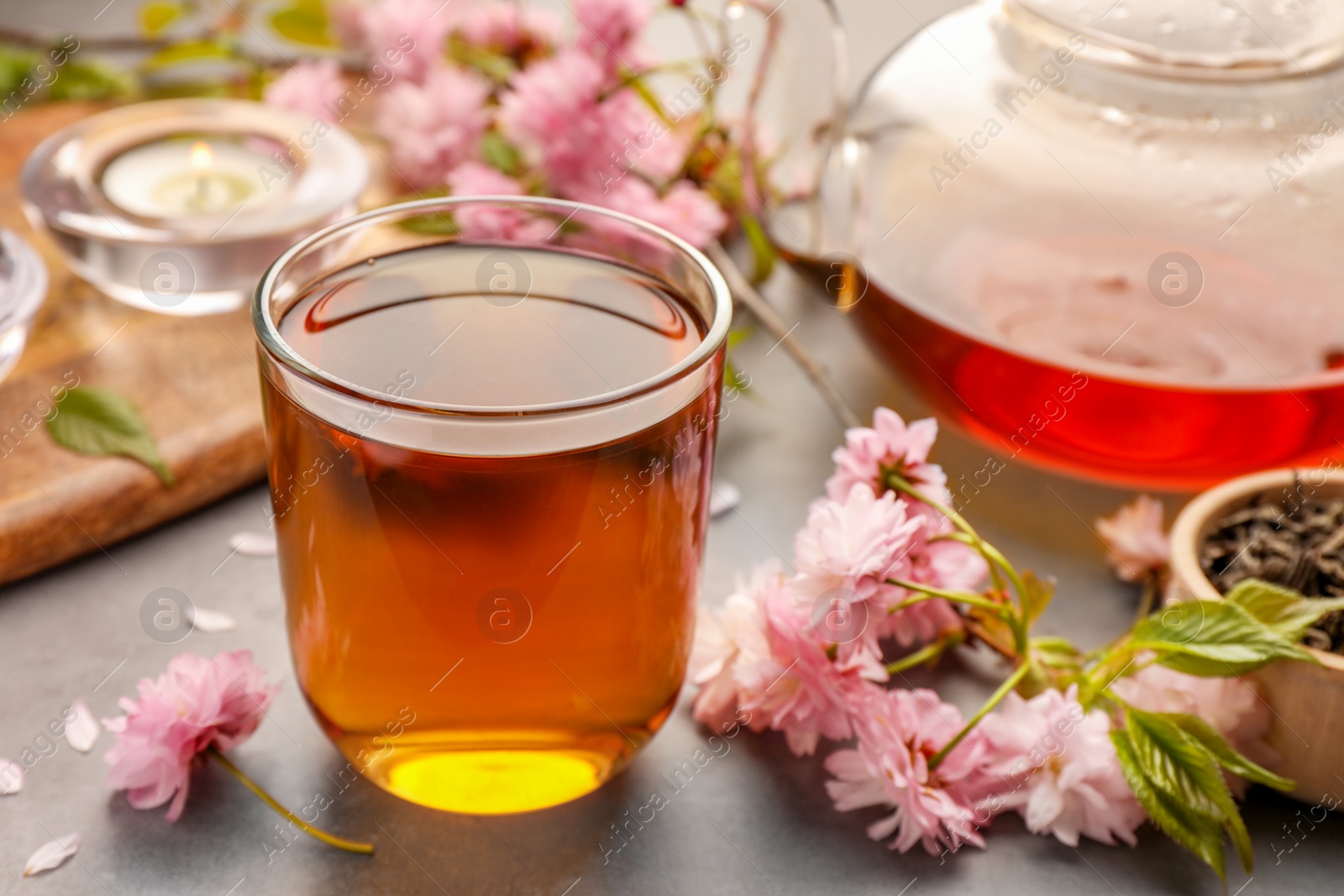 Photo of Traditional ceremony. Cup of brewed tea, teapot and sakura flowers on grey table, closeup