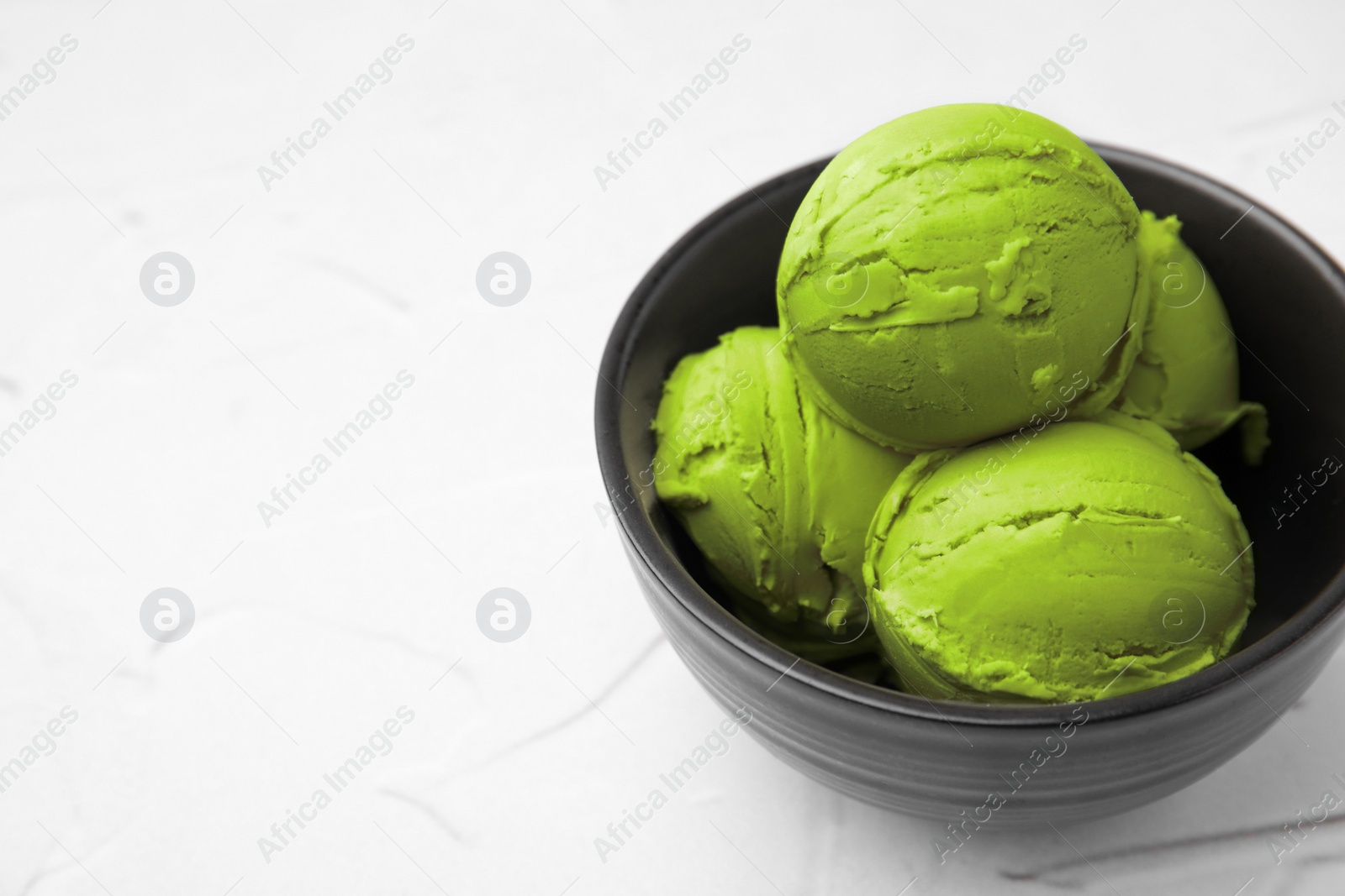 Photo of Tasty matcha ice cream in bowl on white textured table, space for text