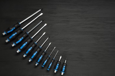 Photo of Set of screwdrivers on black wooden table, top view. Space for text