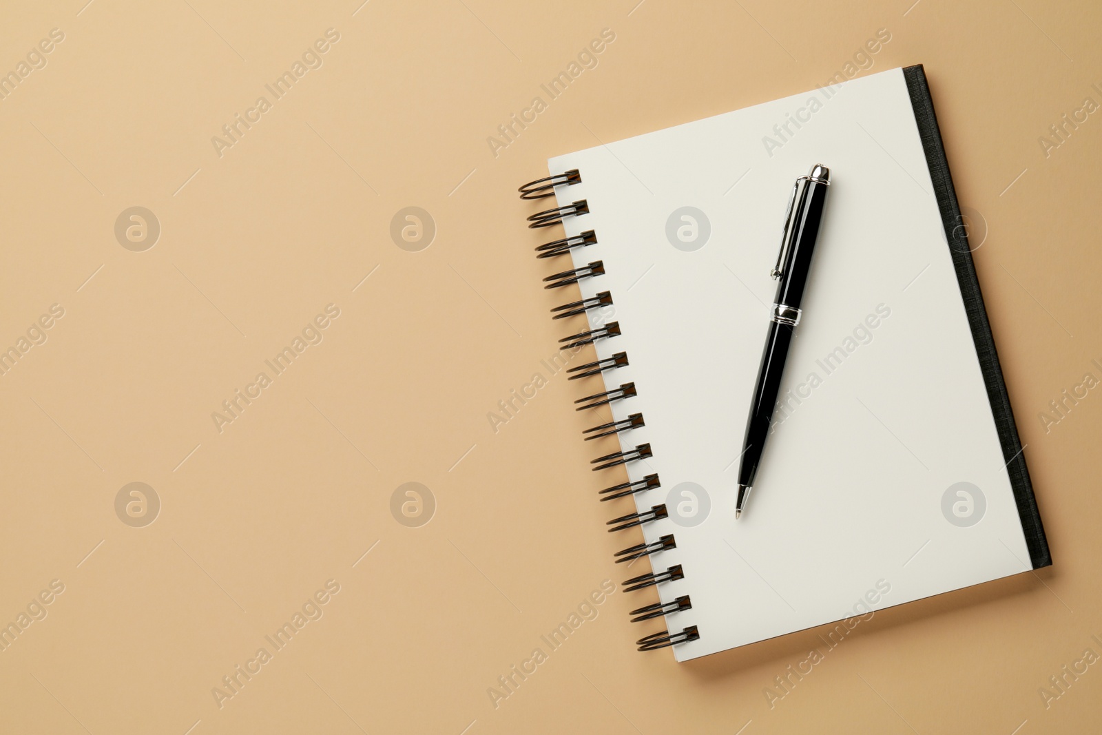 Photo of Notebook and pen on beige background, top view. Space for text