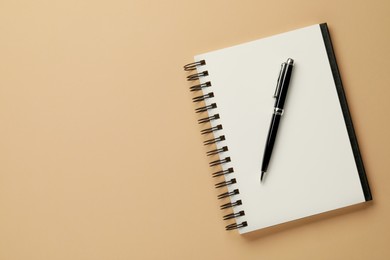 Notebook and pen on beige background, top view. Space for text