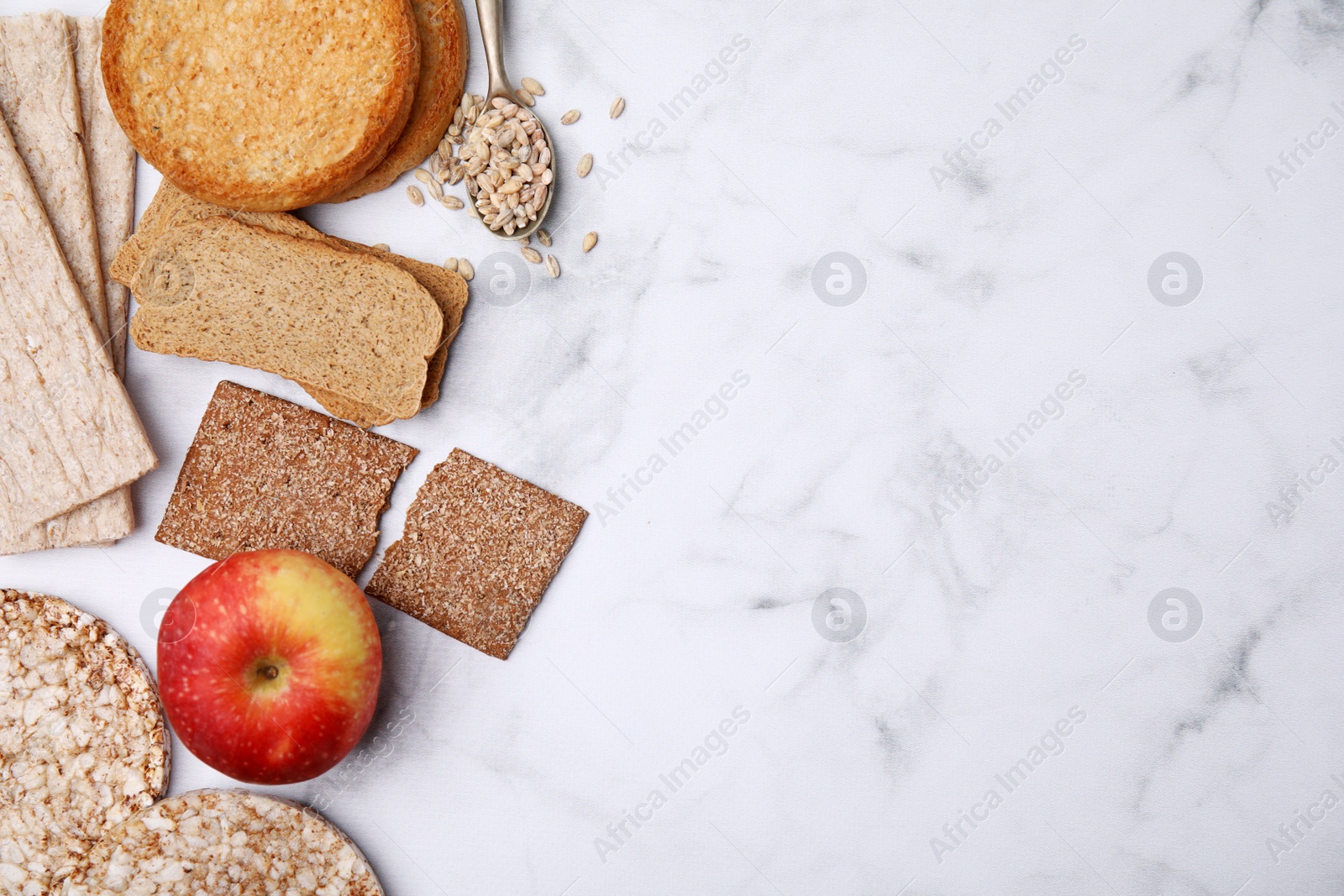 Photo of Rye crispbreads, rice cakes and rusks on white marble table, flat lay. Space for text