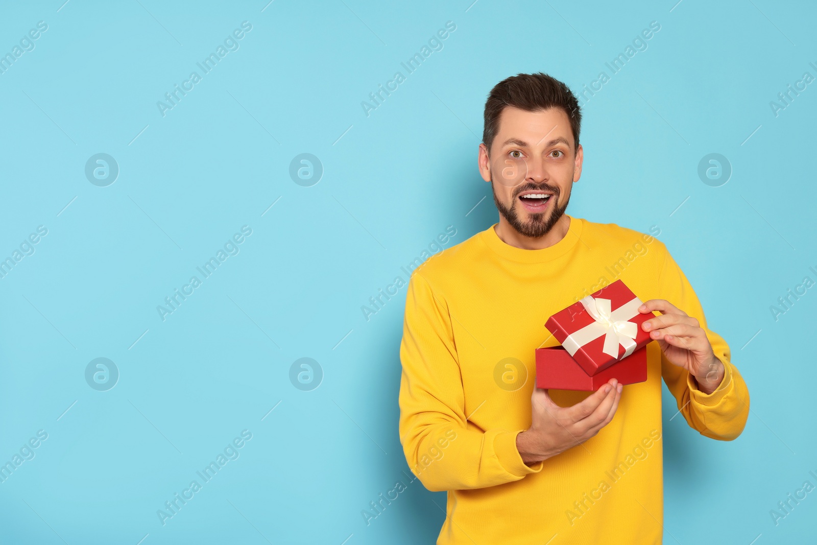 Photo of Happy man with gift box on light blue background, space for text