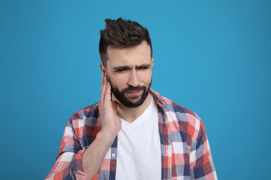 Photo of Man suffering from ear pain on light blue background