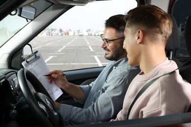 Photo of Driving school. Happy student passing driving test with examiner in car at parking lot