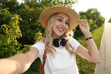 Happy young woman with headphones taking selfie in park on spring day