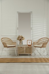 Living room interior with wooden commode, mirror and wicker chairs