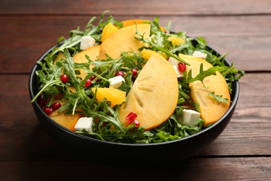 Photo of Delicious persimmon salad with pomegranate and arugula on wooden table