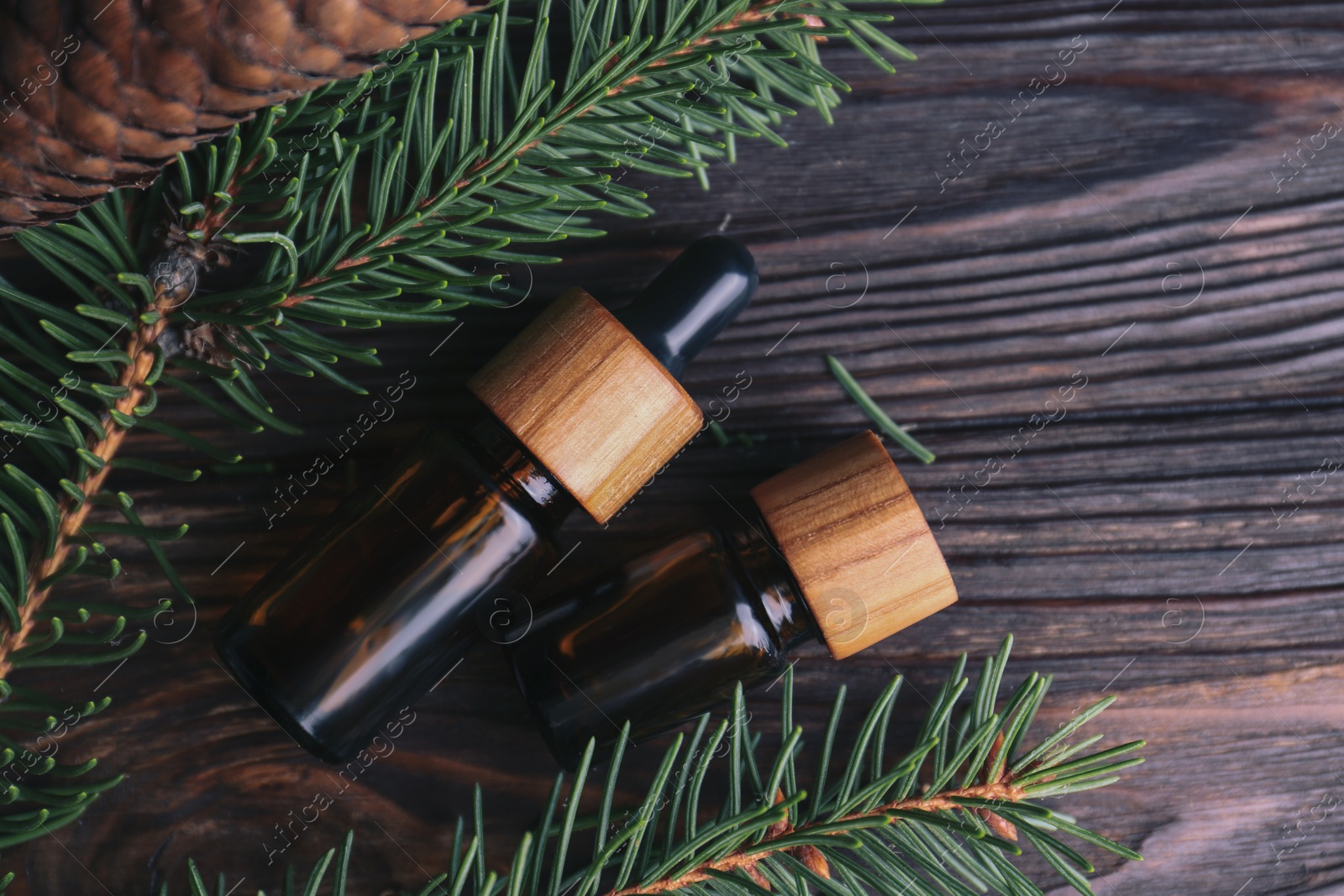 Photo of Bottles of aromatic essential oil, pine branches and cone on wooden table, flat lay