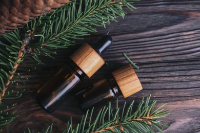 Photo of Bottles of aromatic essential oil, pine branches and cone on wooden table, flat lay