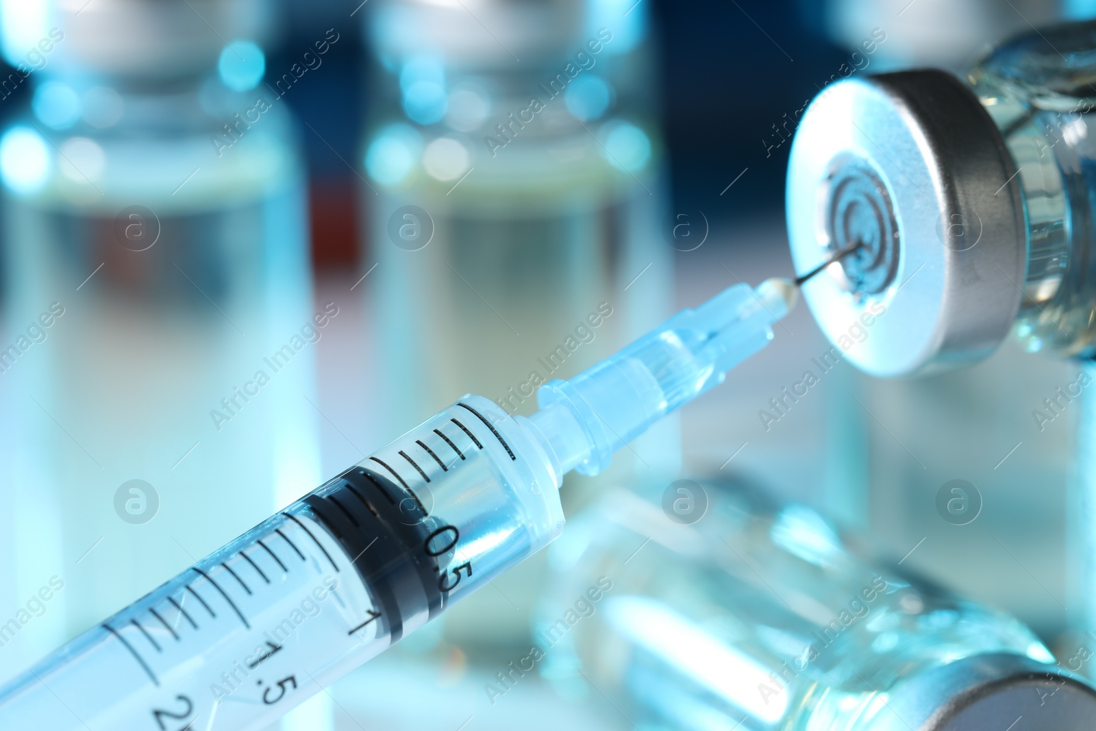 Photo of Filling syringe with medicine from vial against blurred background, closeup