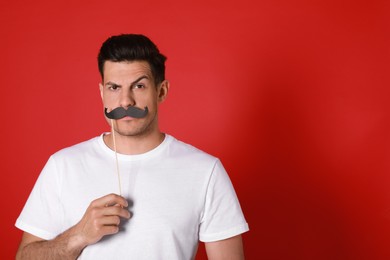 Funny man with fake mustache on red background. Space for text