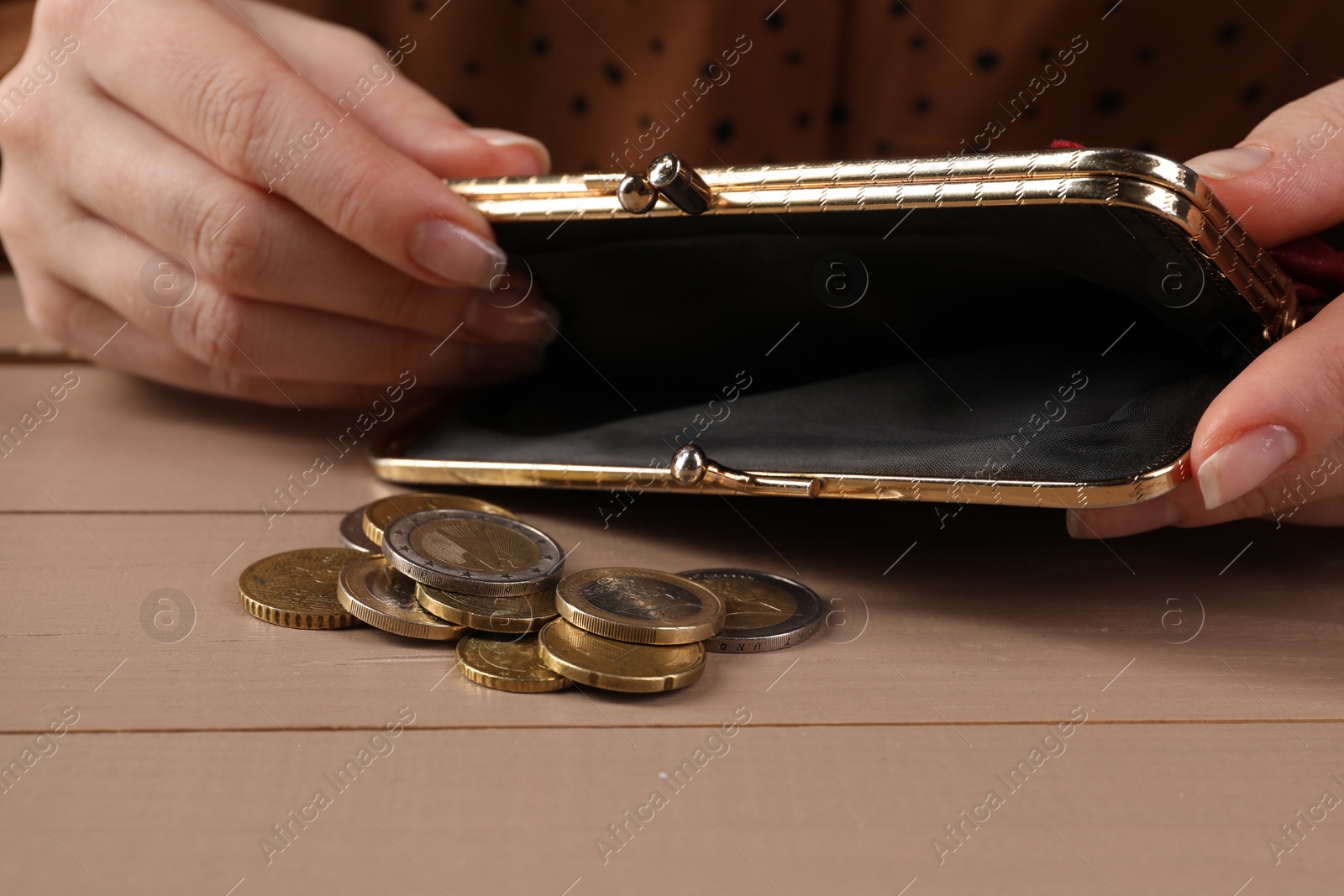 Photo of Poverty. Woman with empty wallet and coins at wooden table, closeup