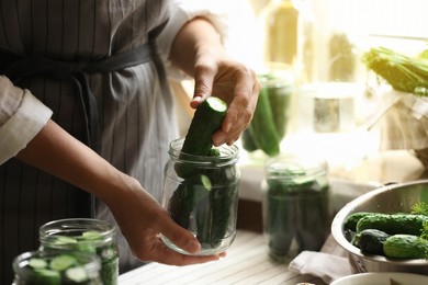 Woman putting cucumbers into jar in kitchen, closeup. Canning vegetables