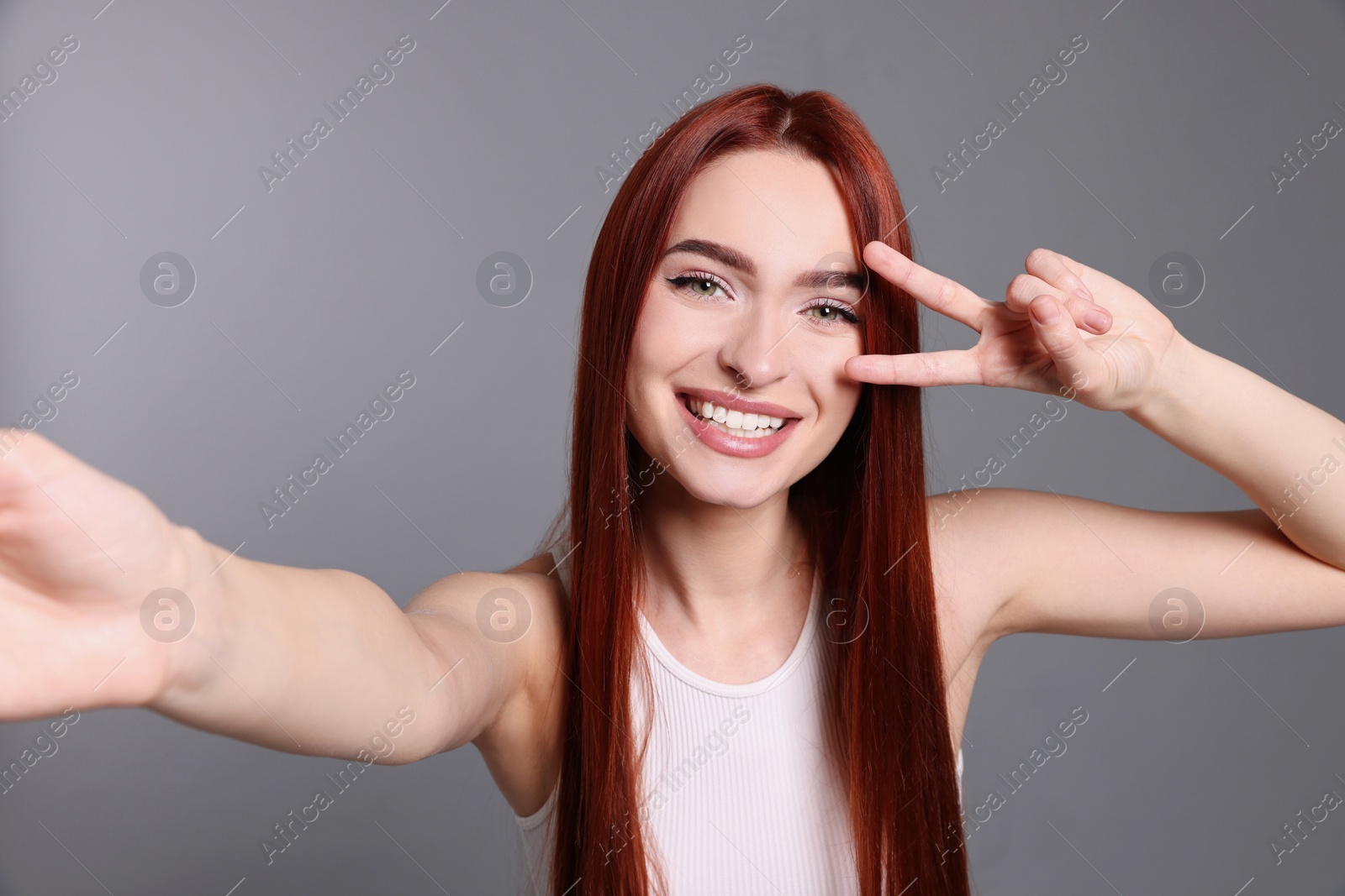 Photo of Happy woman with red dyed hair taking selfie on light gray background