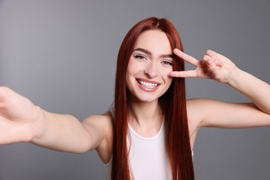 Photo of Happy woman with red dyed hair taking selfie on light gray background