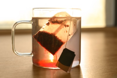 Photo of Tea bag in cup of hot water on wooden table, closeup