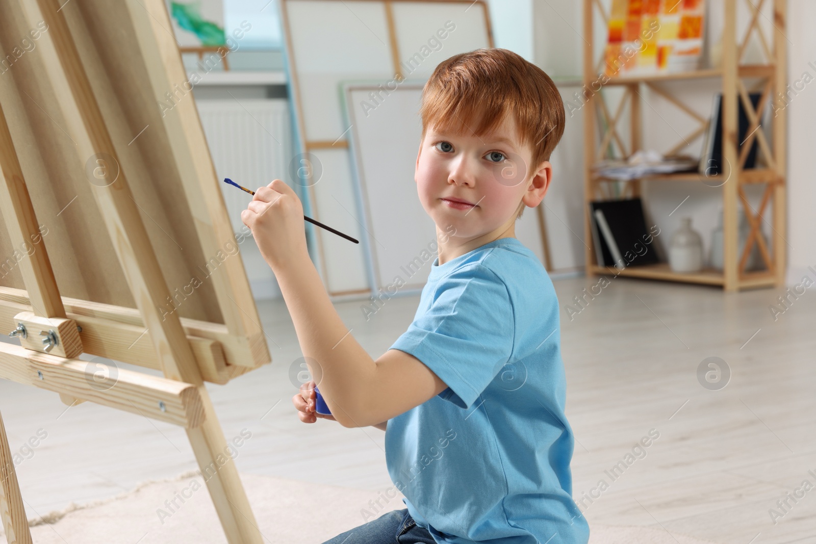 Photo of Little boy painting in studio. Using easel to hold canvas