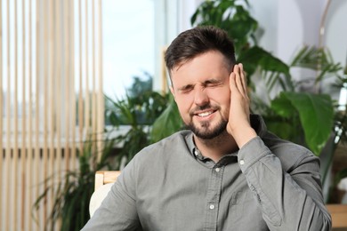 Photo of Young man suffering from ear pain at home. Space for text