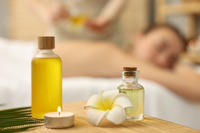 Photo of Aromatherapy. Woman receiving back massage in spa salon, focus on bottles of essential oils and burning candle
