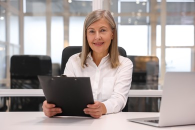 Photo of Smiling woman with clipboard working in office. Lawyer, businesswoman, accountant or manager