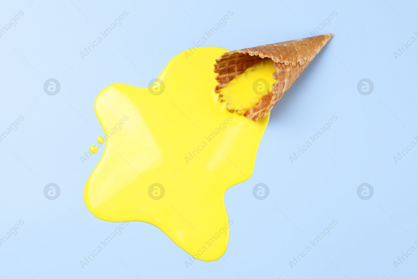 Photo of Melted ice cream and wafer cone on light blue background, top view