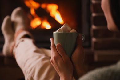 Photo of Woman with cup of sweet cocoa near fireplace indoors, closeup