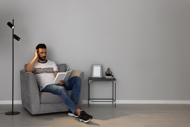 Photo of Man reading book in armchair near gray wall, space for text