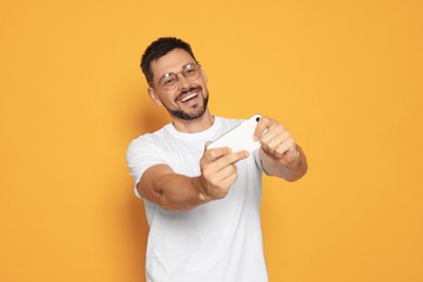 Photo of Emotional man playing game on smartphone against orange background