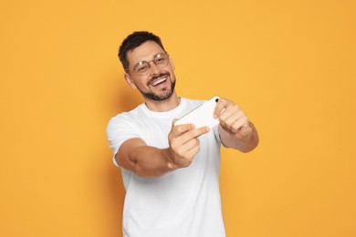 Emotional man playing game on smartphone against orange background