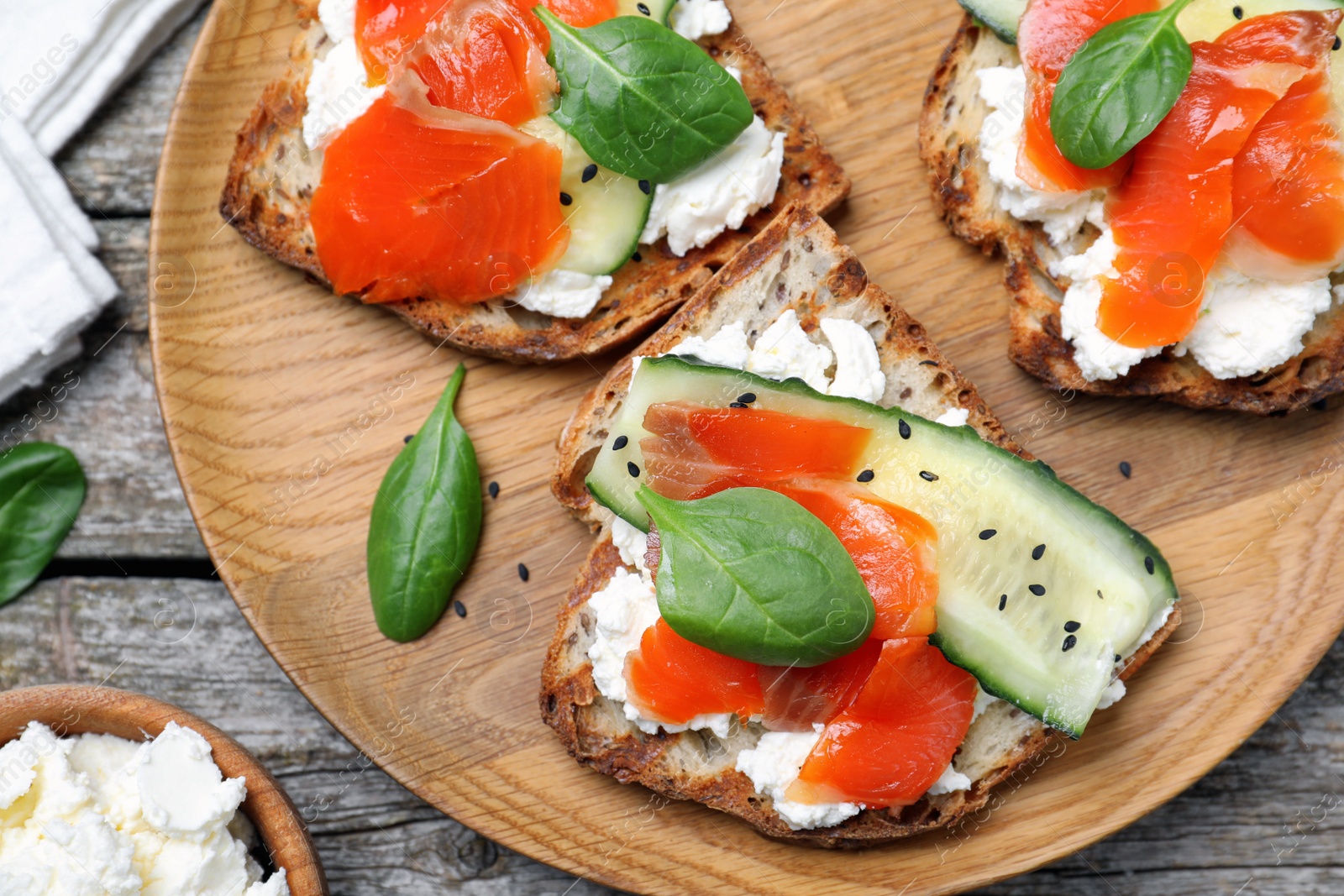 Photo of Delicious sandwiches with cream cheese, salmon, cucumber and spinach served on wooden table, flat lay