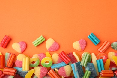 Many different jelly candies on orange background, flat lay. Space for text