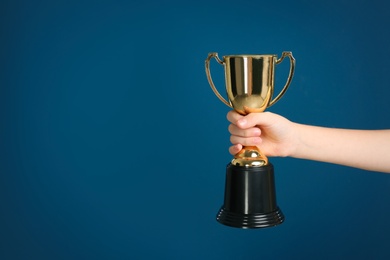 Photo of Child holding golden winning cup on dark blue background, closeup. Space for text