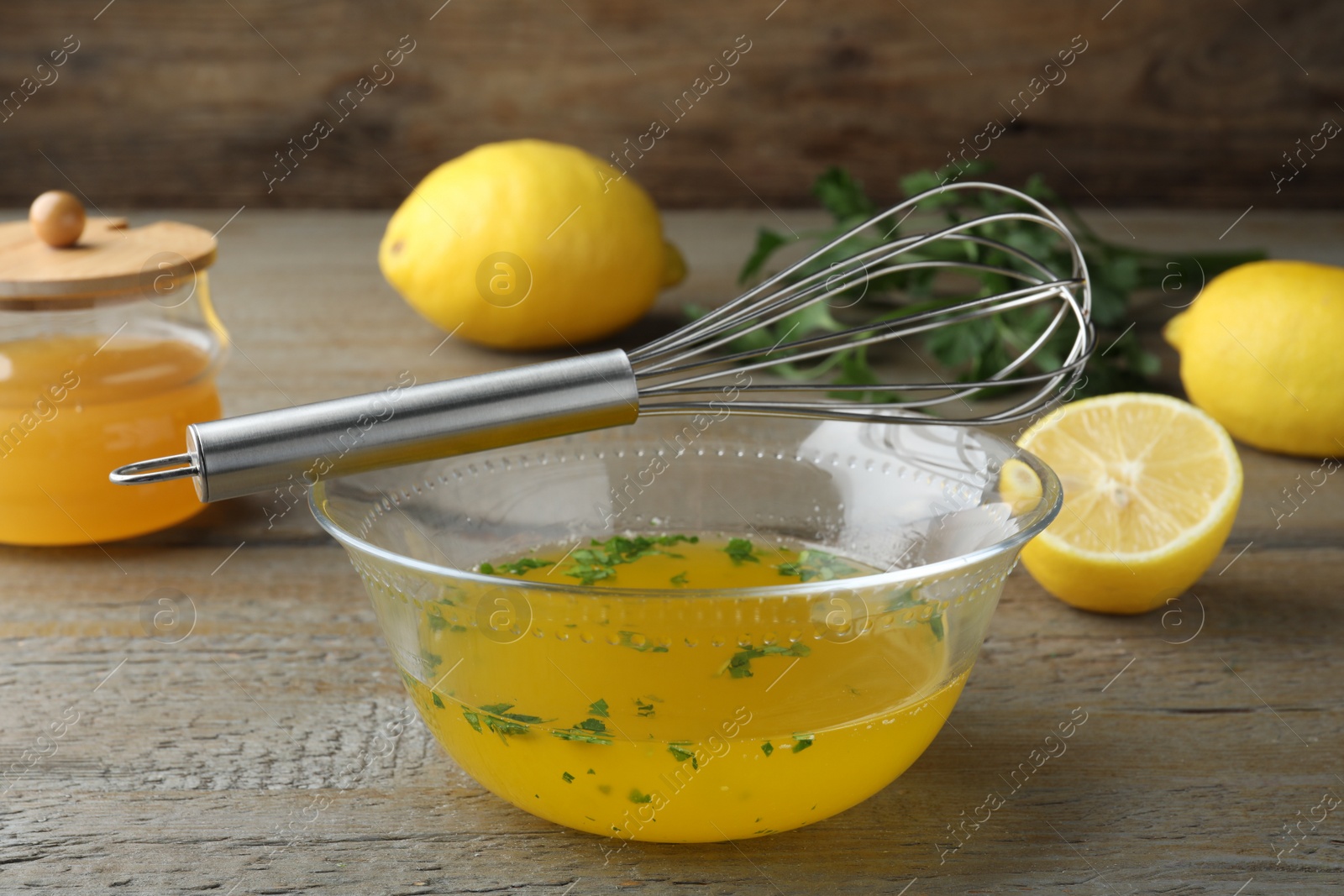 Photo of Whisk and bowl with lemon sauce on wooden table. Delicious salad dressing